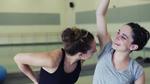 Two young girls in a gym. One is smelling the others armpit