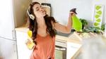 Young woman with headphones on in the kitchen listening to music while cleaning.