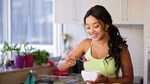 A woman in eating a spoonful of fruits against a kitchen background.