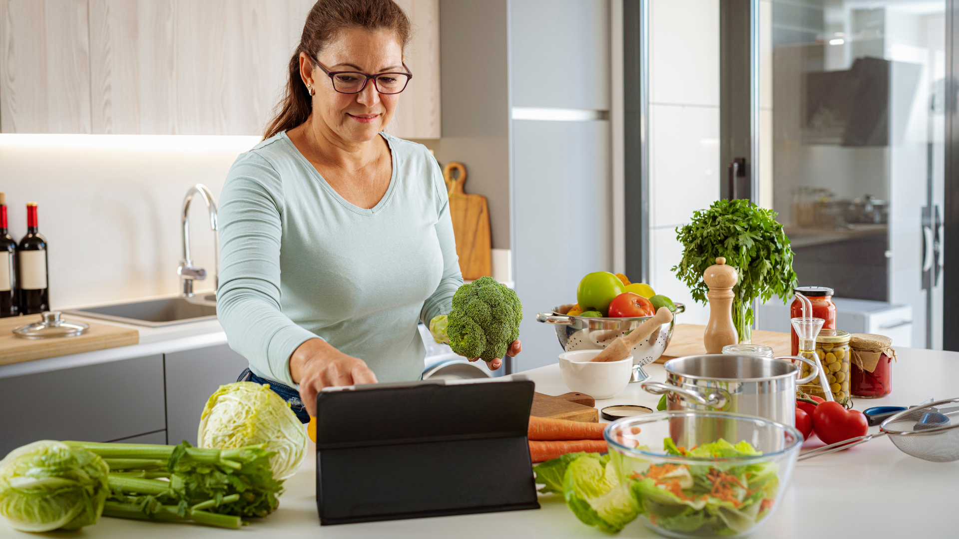 Woman in kitchen using tablet with fresh vegetables around.