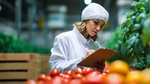 Woman in lab coat inspecting produce in greenhouse.