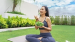 A happy woman in gym clothes is sitting on a mat eating a salad bowl.