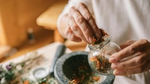 Person holding jar of dried herbs.