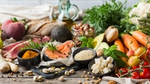 Assorted healthy foods including salmon, vegetables, fruits, and spices on a wooden table.
