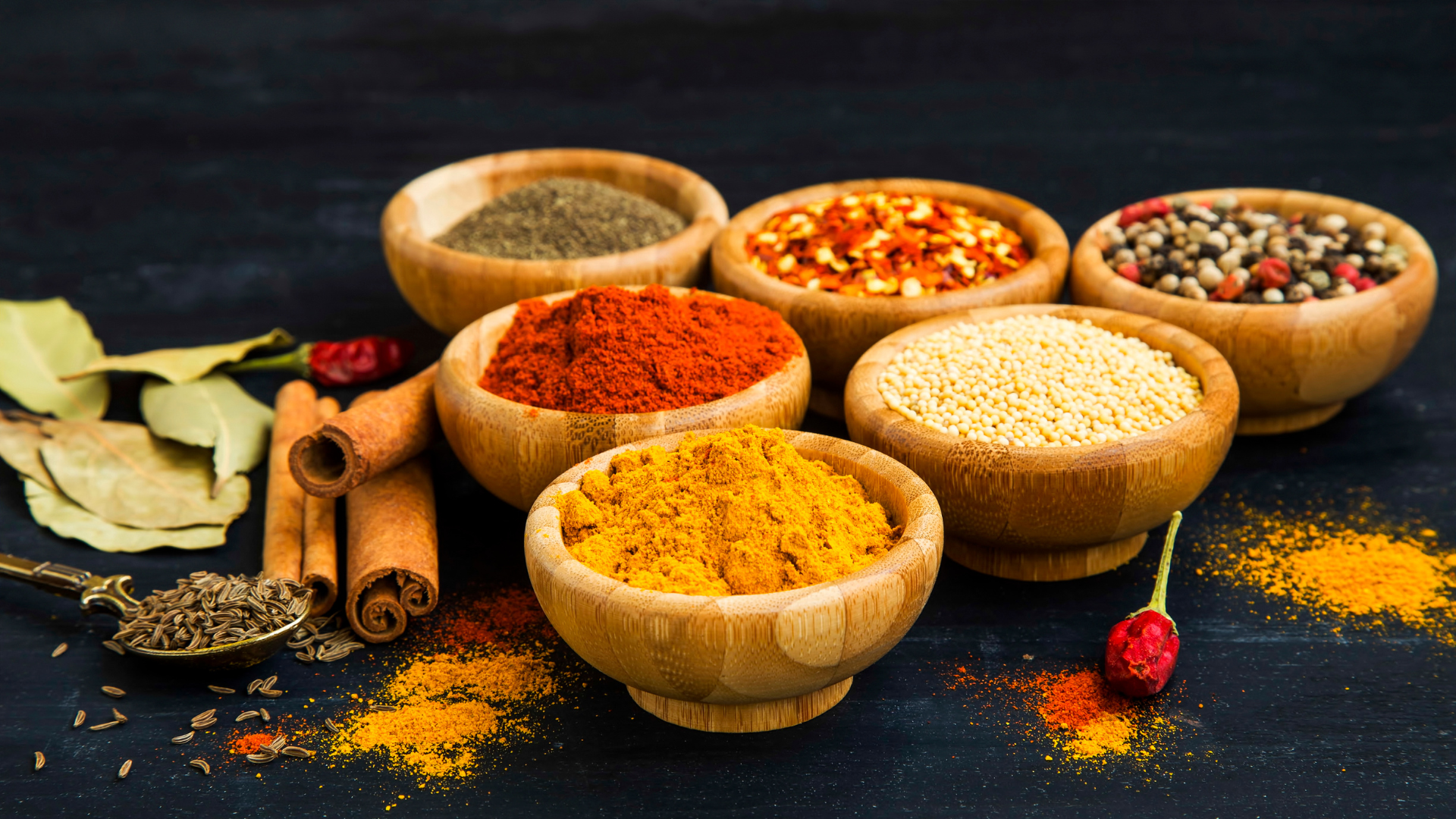 Assorted spices in wooden bowls on a dark background.