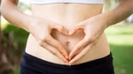 A woman making a heart shape with her hands in front of her gut.