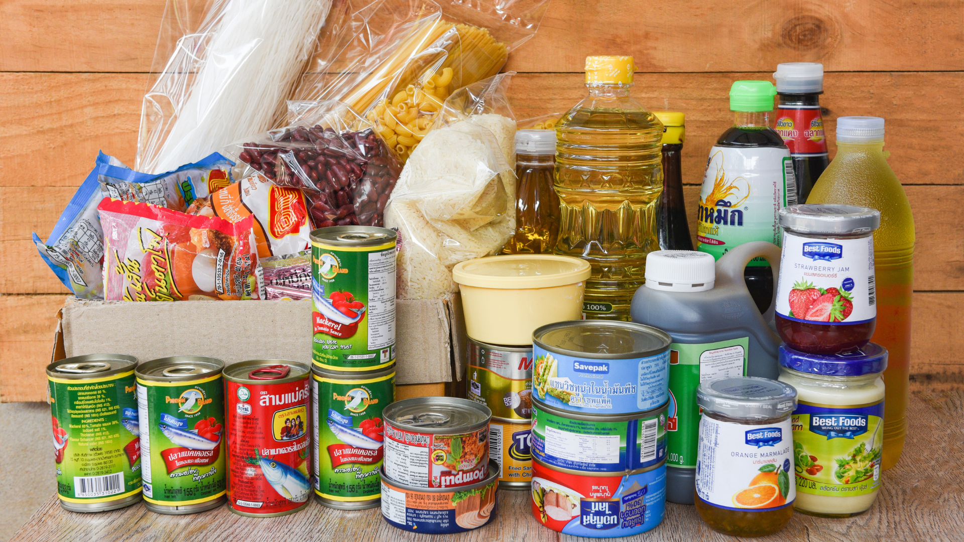 Assorted packaged food items including cans, bottles, and bags on a wooden surface.