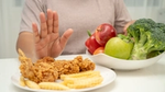 Hand rejecting fried chicken and fries, opting for fruits and vegetables.