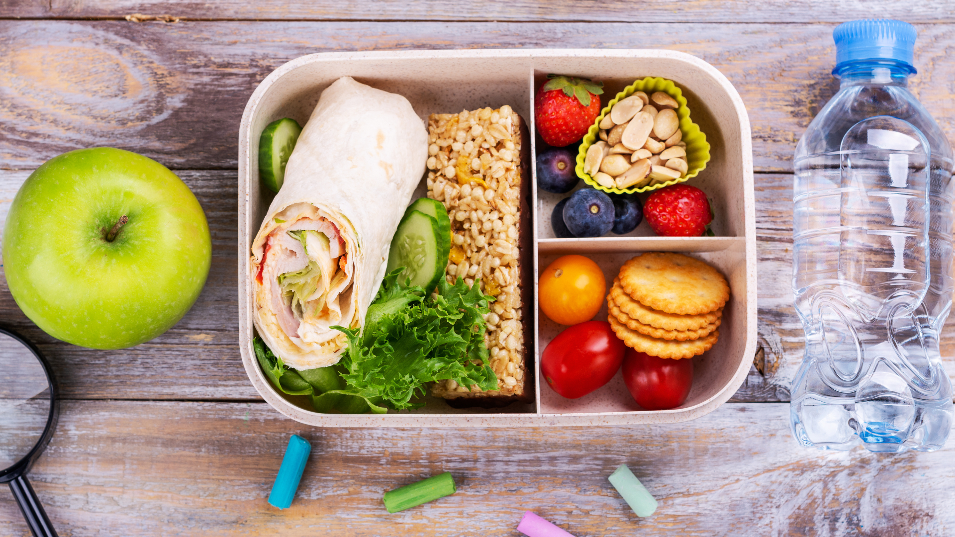 Lunchbox with wrap, nuts, berries, and a green apple on wooden table.