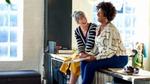 Two women sitting on a worktop chatting and laughing.