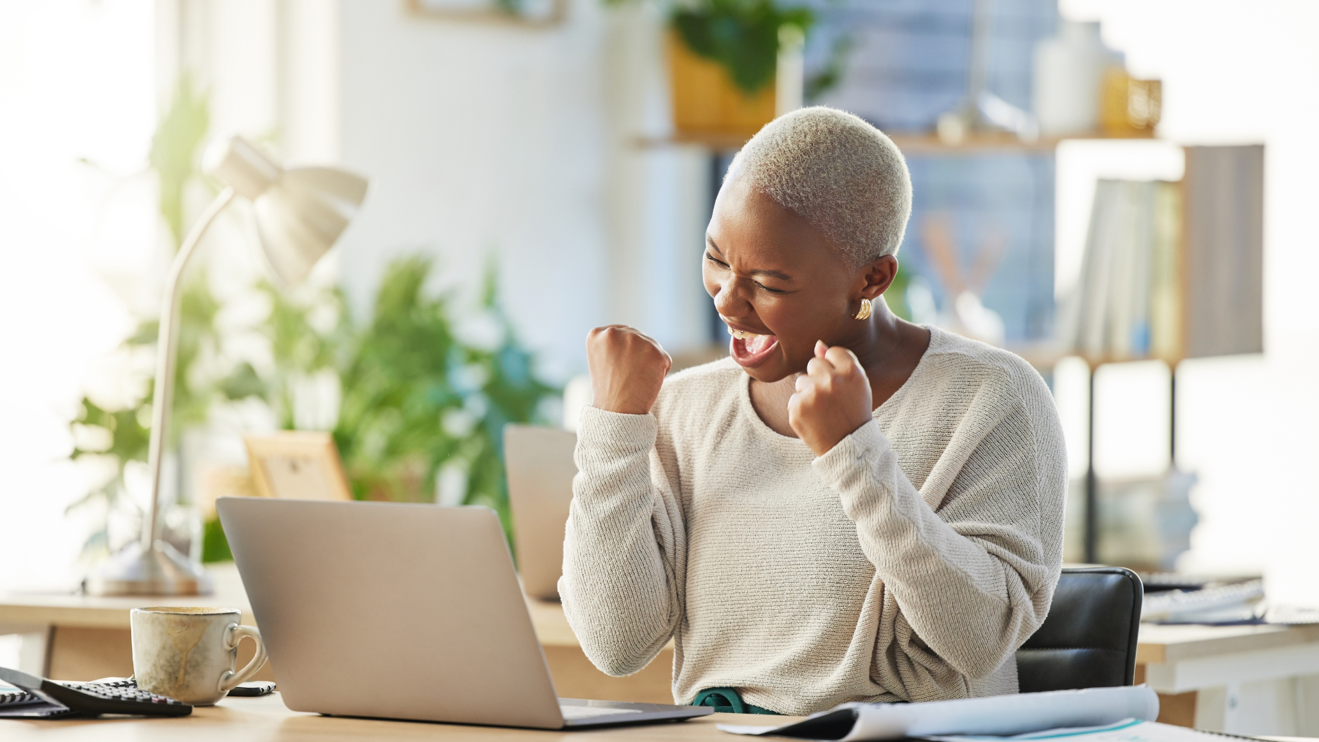 Person celebrating success at a laptop in a bright, cozy office.