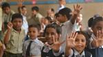 Children in a classroom raise their hands and smile at the camera. They have taken part in a Lifebuoy handwashing lesson, learning how to wash their hands with soap.