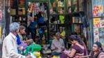 Three men and three women in saris sit outside a small store in rural India, surrounded by colourful products.
