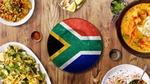South African flag plate surrounded by diverse dishes on a wooden table.
