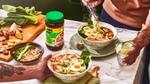 A table laid with two bowls of ramen noodles, a chopping board of ingredients and a jar of Knorr chicken bouillon.